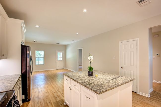 Kitchen with appliances with stainless steel finishes, light wood-type flooring, a kitchen island, stone countertops, and white cabinets | Image 14