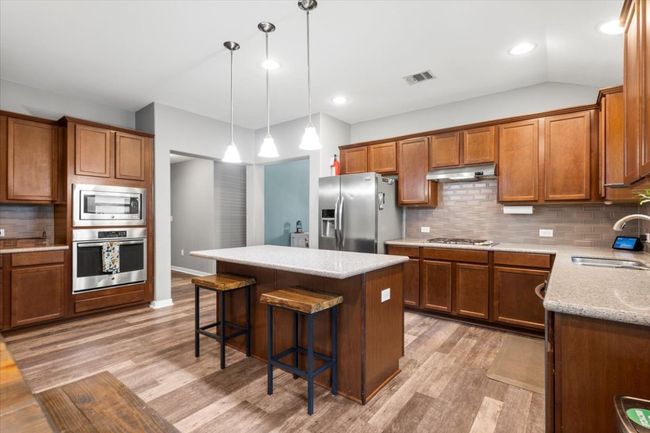 Kitchen with stainless steel appliances, a sink, light wood laminate floors, brown cabinetry, and recessed lighting | Image 11