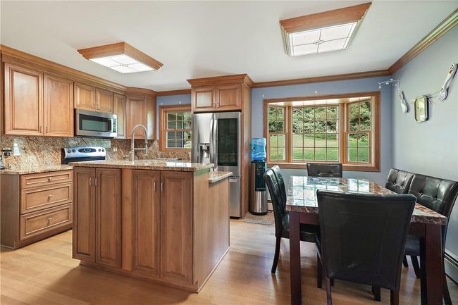 Kitchen featuring decorative backsplash, light wood-type flooring, ornamental molding, light stone counters, and appliances with stainless steel finishes | Image 10