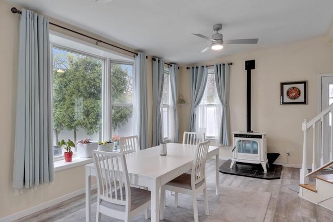 Dining area featuring light wood finished floors, a wood stove, stairway, and ceiling fan | Image 26