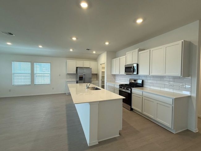 Kitchen featuring appliances with stainless steel finishes, a sink, decorative backsplash, light wood-style flooring, and a kitchen island with sink | Image 23