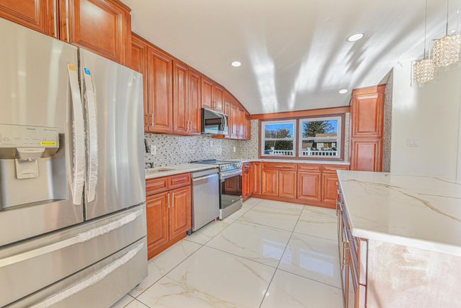 Kitchen featuring appliances with stainless steel finishes, pendant lighting, light stone counters, and decorative backsplash | Image 20