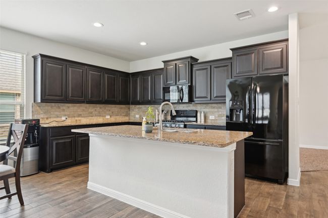 Kitchen featuring black appliances, light wood-style flooring, light stone countertops, tasteful backsplash, and recessed lighting | Image 10