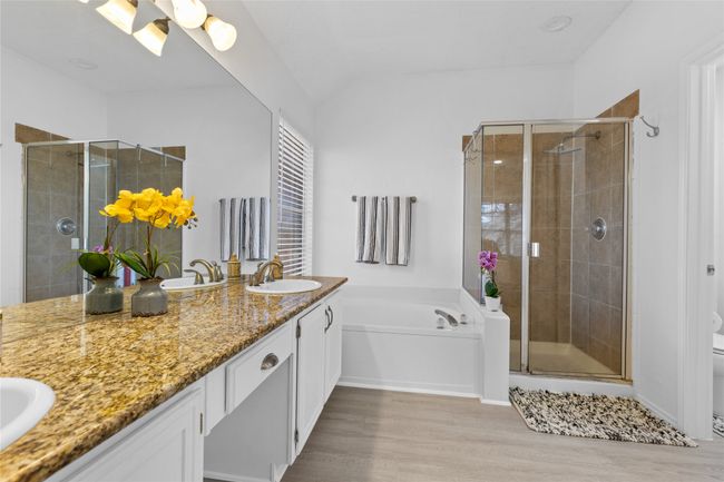Full bathroom featuring double vanity, a shower stall, wood finished floors, a bath, and lofted ceiling | Image 12