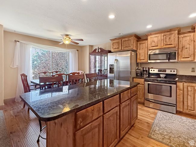 Kitchen featuring appliances with stainless steel finishes, dark stone counters, a breakfast bar area, light wood-style floors, and recessed lighting | Image 6