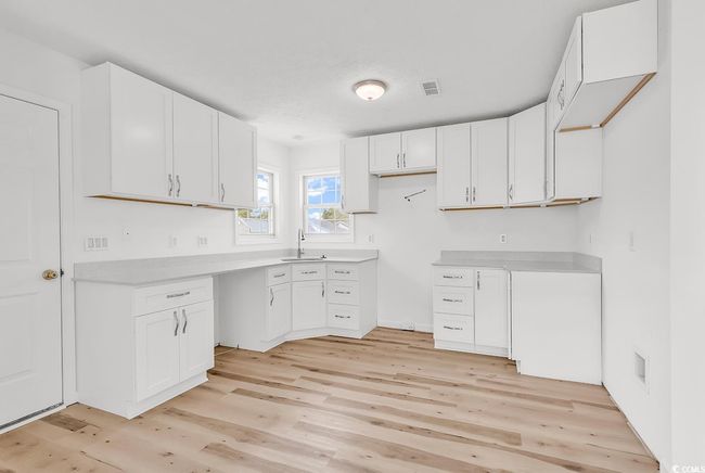 Kitchen featuring white cabinets, light countertops, a sink, and light wood-style floors | Image 4