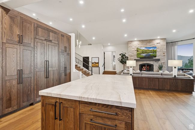 Kitchen featuring light wood-type flooring, a kitchen island, a fireplace, vaulted ceiling, and light stone counters | Image 26