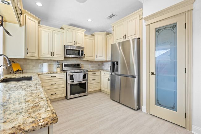 Kitchen with stainless steel appliances, cream cabinetry, light stone countertops, light wood-type flooring, and tasteful backsplash | Image 6