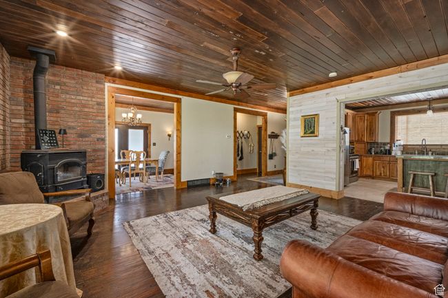 Living area with wooden ceiling, a wood stove, ceiling fan, baseboards, and wood walls | Image 5