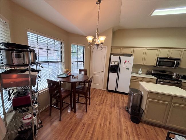 Kitchen with appliances with stainless steel finishes, vaulted ceiling, light countertops, light wood-style floors, and a chandelier | Image 5