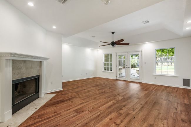 Unfurnished living room with wood finished floors, a fireplace, a ceiling fan, french doors, and recessed lighting | Image 9