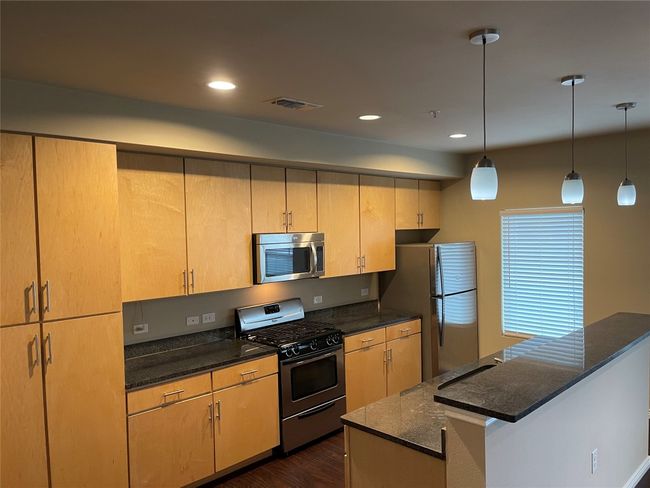 Kitchen featuring stainless steel appliances, dark wood-type flooring, dark stone countertops, recessed lighting, and decorative light fixtures | Image 13