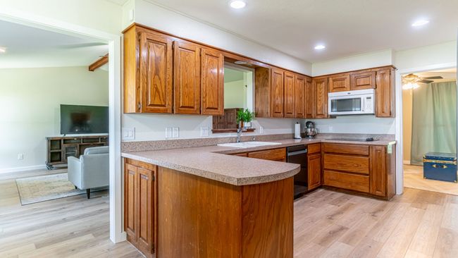 Kitchen with white microwave, dishwashing machine, a sink, brown cabinets, and light wood finished floors | Image 12