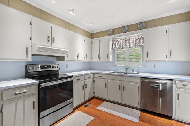 Kitchen with under cabinet range hood, stainless steel appliances, light countertops, visible vents, and a sink | Image 7