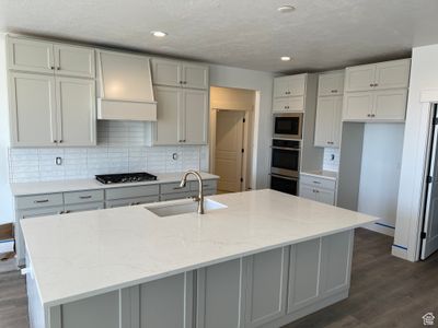 Kitchen with light stone countertops, a center island with sink, sink, and dark hardwood / wood-style flooring | Image 3