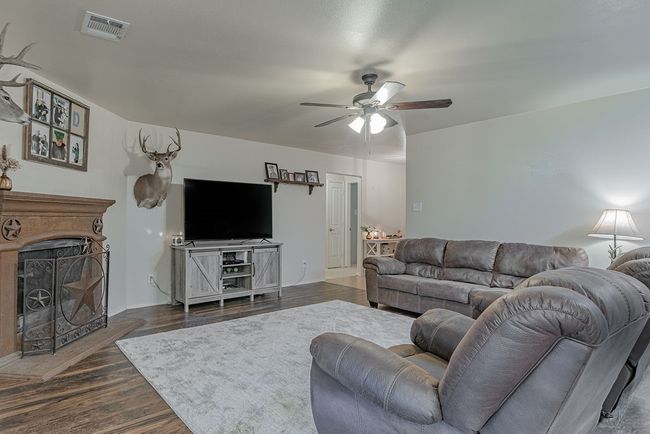 Living room featuring visible vents, a fireplace with raised hearth, dark wood-type flooring, and a ceiling fan | Image 8