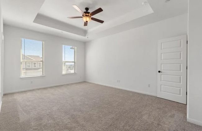 Empty room featuring a tray ceiling, carpet flooring, a ceiling fan, and baseboards | Image 8