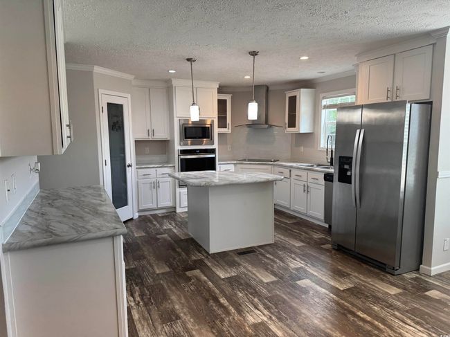 Kitchen featuring appliances with stainless steel finishes, wall chimney range hood, dark wood-style floors, crown molding, and recessed lighting | Image 11