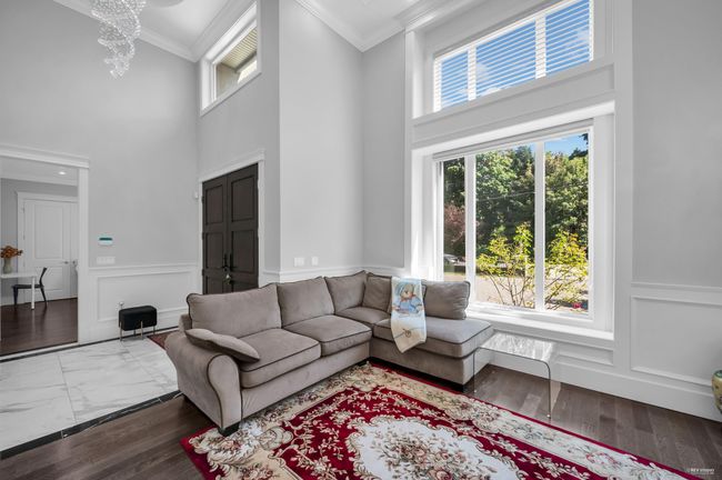 Living room featuring healthy amount of natural light, a high ceiling, ornamental molding, a chandelier, and a wainscoted wall | Image 5