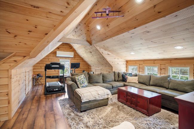 Living room featuring wooden ceiling, lofted ceiling with beams, wooden walls, a wall unit AC, and wood finished floors | Image 26