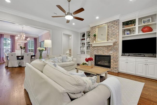 The spacious family room is the heart of the home, seamlessly open to the dining area and designed for both comfort and entertaining. A striking Heatilator gas log fireplace serves as the focal point, featuring a floor-to-ceiling brick surround with a rich wood mantle, perfectly framed by custom built-ins on either side—ideal for media, books, or decorative displays. | Image 10