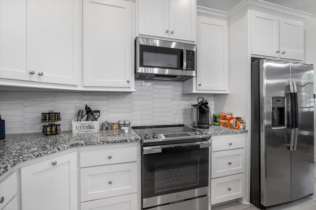 Kitchen featuring tasteful backsplash, white cabinetry, stainless steel appliances, and light stone countertops | Image 11