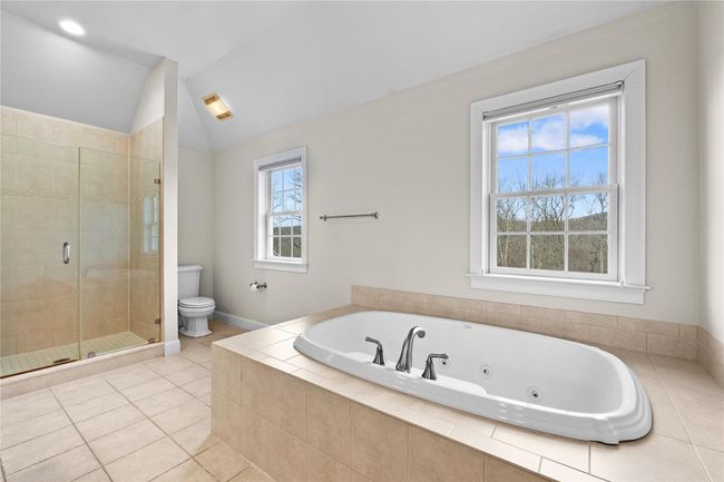 Bathroom with toilet, a jetted tub, vaulted ceiling, tile patterned flooring, and a stall shower | Image 27