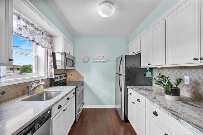 Kitchen with stainless steel appliances, dark wood-type flooring, white cabinets, decorative backsplash, and light stone counters | Image 13