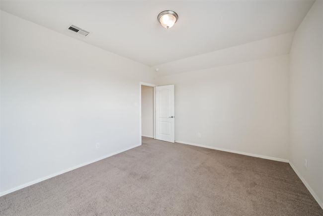 This photo shows a clean, bright, and upstairs bedroom 1 featuring neutral painted walls and carpet. It includes a ceiling light and a white door, ideal for a bedroom or office. | Image 21