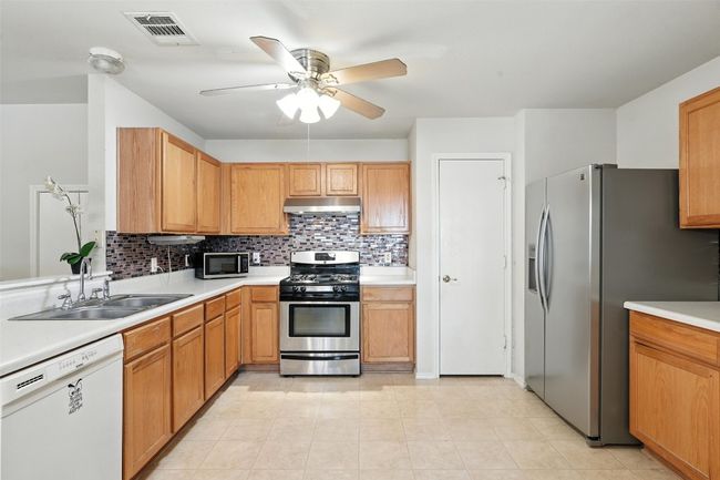 Kitchen with backsplash, stainless steel appliances, light countertops, and light tile patterned floors | Image 12