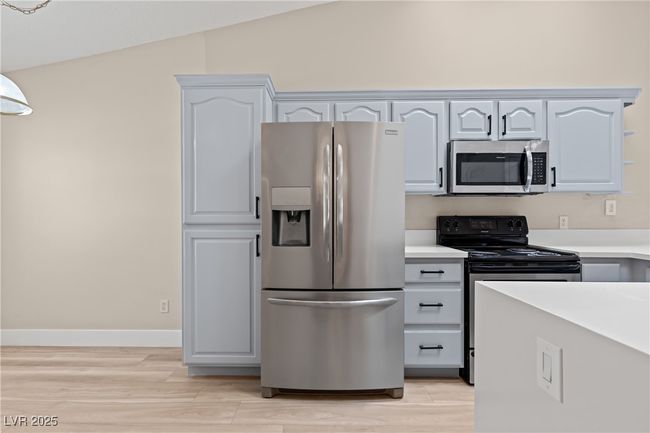 Kitchen featuring stainless steel appliances, light countertops, light wood finished floors, white cabinetry, and pendant lighting | Image 14