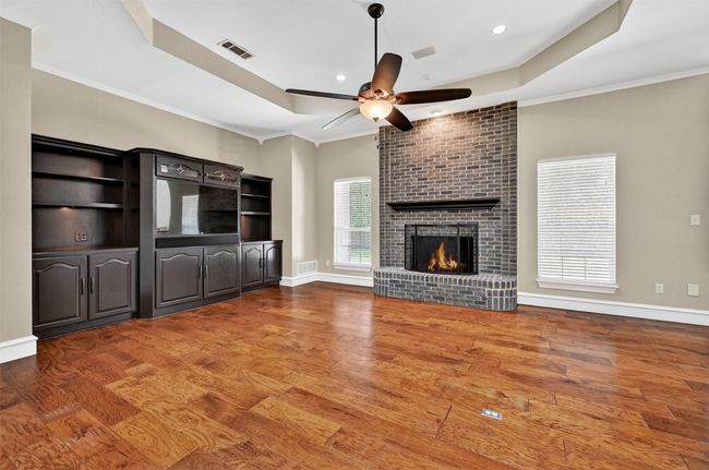 Unfurnished living room with ceiling fan, wood finished floors, a fireplace, a raised ceiling, and ornamental molding | Image 11
