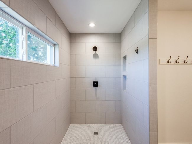 Huge shower with elegant tile, recesses for soap and shampoo keep the area looking sleek. Beautifully detailed shower floor tile has a subtle leaf pattern. Windows allow for natural light while maintaining privacy. Notice the well placed recessed light. | Image 19