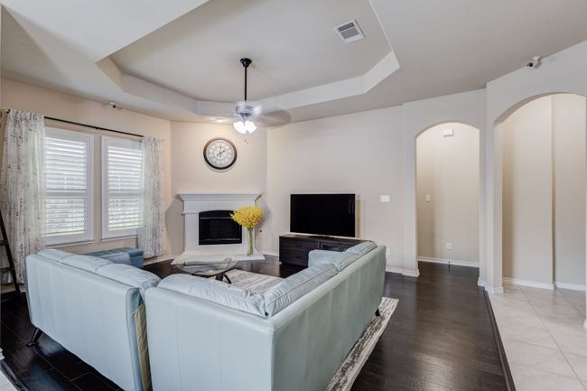 Living room featuring a tray ceiling, a fireplace with raised hearth, arched walkways, and wood finished floors | Image 9