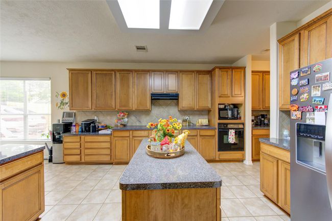 Bright, spacious kitchen with ample natural light, featuring wooden cabinetry, granite countertops, tile flooring, and modern appliances. A central island provides extra workspace and storage, perfect for cooking and entertaining. | Image 10