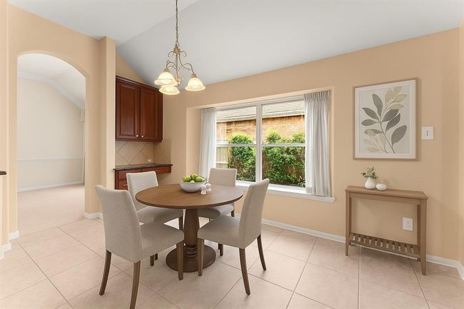 The bright and airy breakfast room is framed by a large picture window overlooking lush greenery, creating a cheerful start to your day. A built-in desk or serving station adds both charm and functionality, making this space ideal for casual meals or morning coffee. Virtually staged | Image 13
