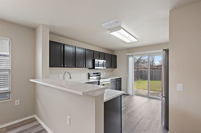 Kitchen with light wood-style floors, appliances with stainless steel finishes, light countertops, a peninsula, and dark cabinetry | Image 8