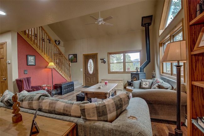Living room with a wood stove, high vaulted ceiling, stairs, a ceiling fan, and wood finished floors | Image 12