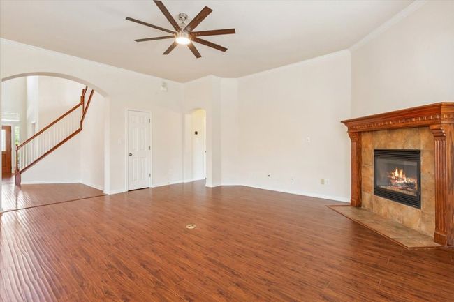 Unfurnished living room with ceiling fan, a tiled fireplace, arched walkways, crown molding, and wood finished floors | Image 9