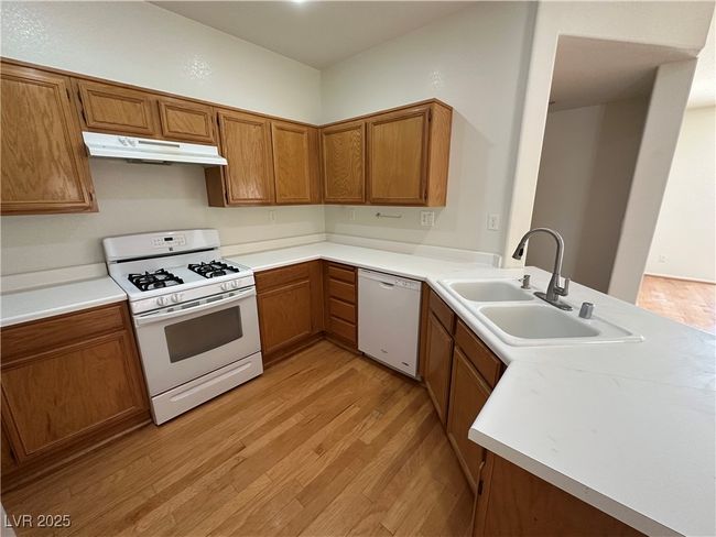 Kitchen featuring white appliances, under cabinet range hood, a sink, and light wood-type flooring | Image 13