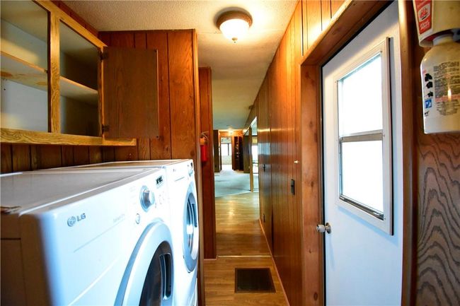 Laundry area with wood-type flooring, a textured ceiling, wooden walls, and independent washer and dryer | Image 21