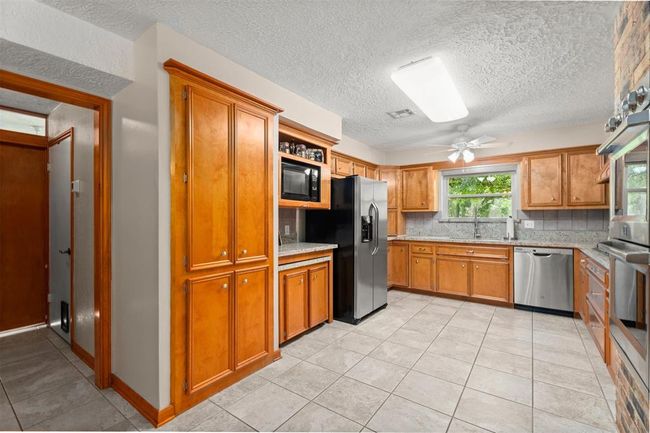 Spacious kitchen with abundant wood cabinetry, granite countertops, and a central island. Includes stainless steel appliances, tile flooring, and a large window providing natural light. | Image 9