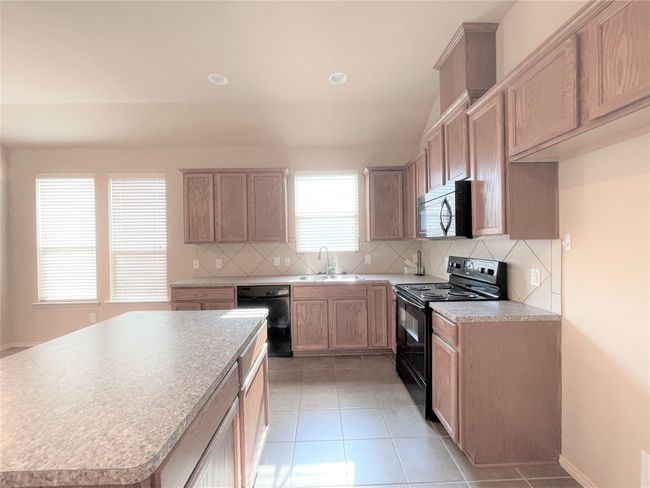 Kitchen with black appliances, light tile patterned floors, tasteful backsplash, light countertops, and a kitchen island | Image 5
