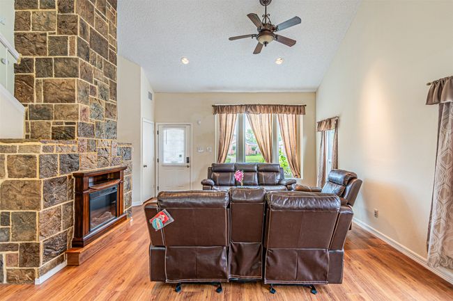 Living room featuring a ceiling fan, a stone fireplace, wood finished floors, a textured ceiling, and high vaulted ceiling | Image 5