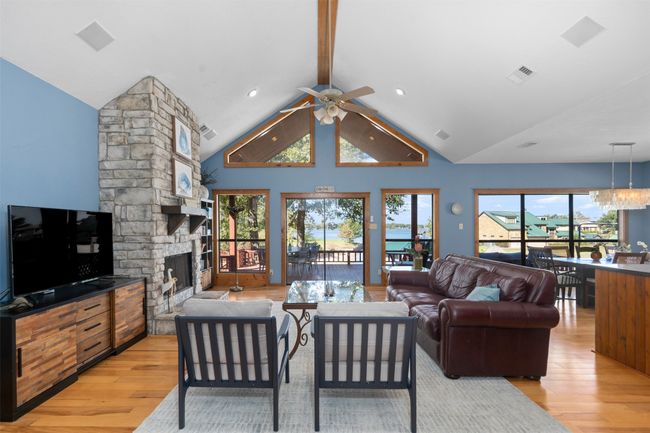 Living room featuring ceiling fan with notable chandelier, light hardwood / wood-style floors, lofted ceiling with beams, and a stone fireplace | Image 6