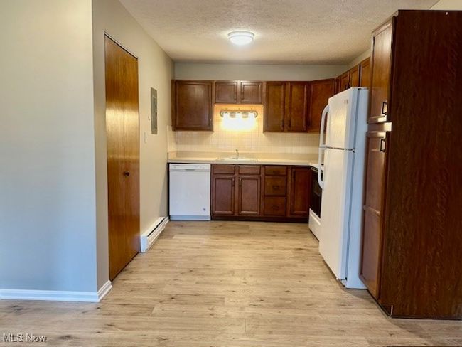 Kitchen with white appliances, a baseboard radiator, a sink, light wood-style floors, and tasteful backsplash | Image 7