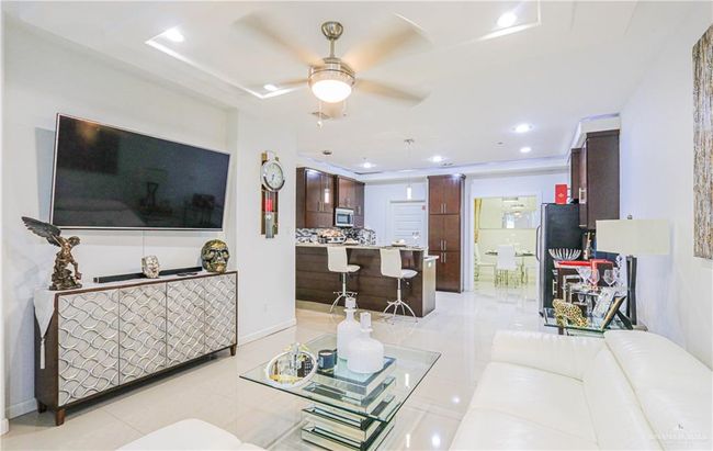 Living room with ceiling fan, a raised ceiling, and light tile patterned floors | Image 7