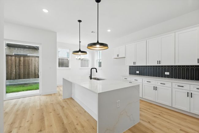 Kitchen featuring a sink, light wood-style flooring, decorative backsplash, white cabinetry, and light stone counters | Image 15