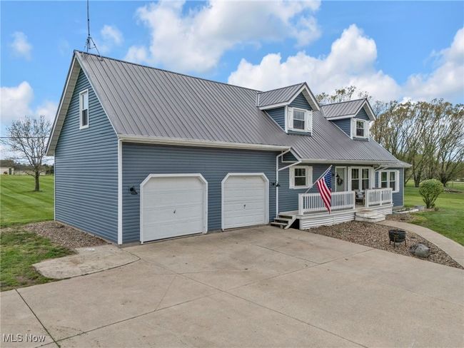 New england style home with a porch, concrete driveway, metal roof, and an attached garage | Image 5
