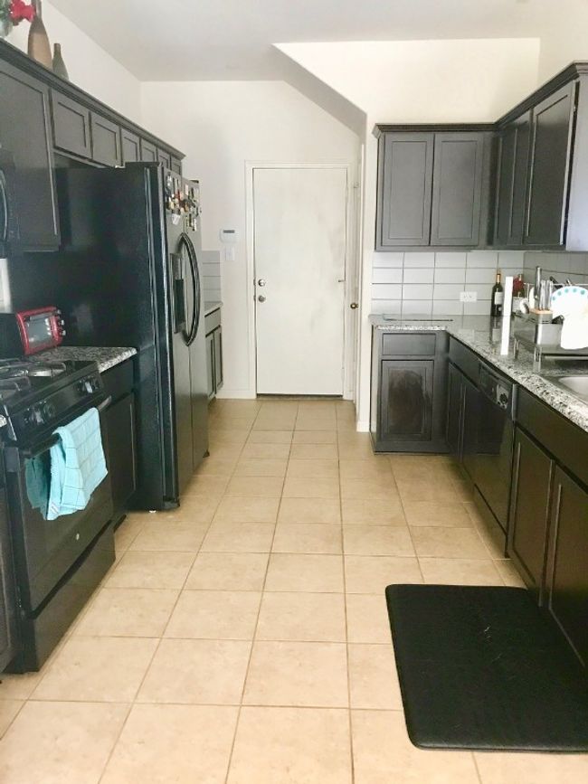 Kitchen with light tile patterned flooring, light stone countertops, decorative backsplash, and black appliances | Image 7